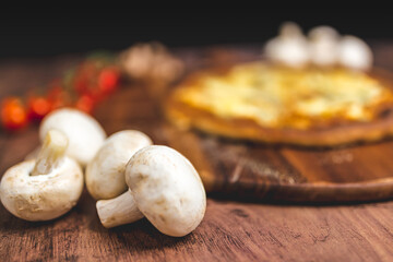 Close-up white mushrooms on a wooden table with pizza in background. Mushroom ingredient for pizza. Concept of preparing pizza with white mushrooms.