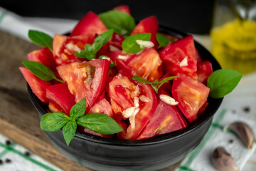 fresh ripe tomato slices and green basil salad in a black bowl on a wooden cutting board
