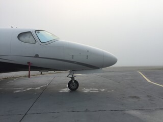 Foggy business jet parked at airport with heavy fog around