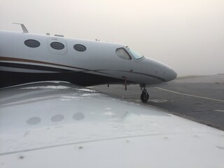 Foggy business jet parked at airport with heavy fog around