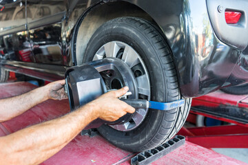 Tyre / tire fitting, rod adjustment. A mechanic man on the a vehicle adjusting the tie-rod to align the wheel correctly.