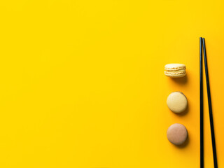 Coffee mocha caramel macarons laid out in vertical row on bright yellow background with black chopsticks. Creative food concept for French pastry confectionery