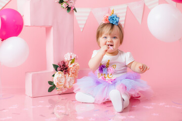 Fototapeta na wymiar Smash cake party. Little cheerful birthday girl with first cake. Happy infant baby celebrating his first birthday. Decoration and photo zone for first year. One year baby celebration. Pink decor.