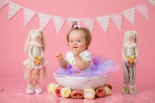 Smash cake party. Little cheerful birthday girl with first cake. Happy infant baby celebrating his first birthday. Decoration and photo zone for first year. One year baby celebration. Pink decor.