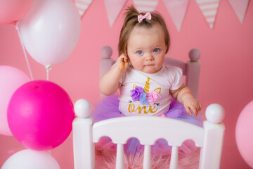 Fototapeta na wymiar Smash cake party. Little cheerful birthday girl with first cake. Happy infant baby celebrating his first birthday. Decoration and photo zone for first year. One year baby celebration. Pink decor.