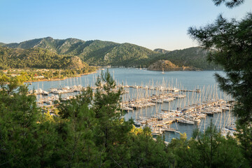 Fototapeta na wymiar Yacht Marina. Footage of many luxury boats and yachts in the harbor. Beautiful forested mountain landscape with the sea in the background. Orhaniye, Hisaronu, Marmaris - TURKEY