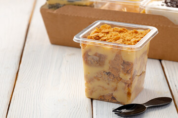 Creamy dessert in a plastic box on wooden table