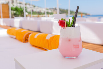 strawberry cocktail in front of a white background. cold pink cocktail with ice on the beach club in hot summer day. cocktail image with foam on the background with sun beds and towels