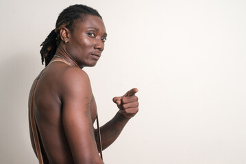 Young handsome muscular African man with dreadlocks pointing finger and looking back shirtless