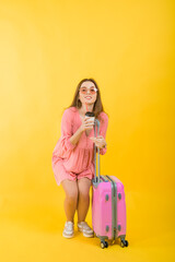 Fototapeta na wymiar Beautiful elegant woman in a pink dress with a pink big suitcase for travel on a yellow isolated background