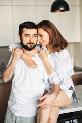Cozy morning at home. Couple in love hug in the kitchen. A young woman and man in homewear cuddle tenderly indoor. Vertical shot