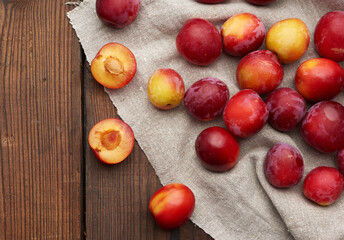 ripe red plums on a gray linen towel, brown wooden table