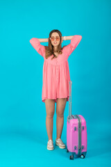 Beautiful elegant woman in a pink dress with a pink big suitcase for travel on a blue isolated background