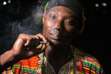 Face of young handsome African Rastafarian man smoking outdoors at night