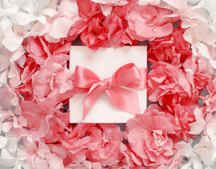 White gift box with a bow between pink flowers
