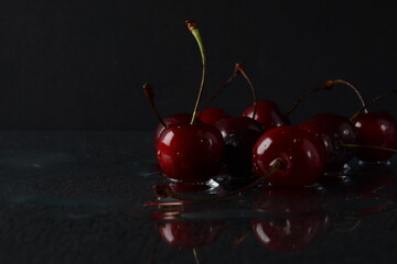 Cherries, with drops of water on a black background with reflection