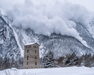 Descent of an avalanche from the mountain. House at the foot of the mountain. Winter mountain landscape.