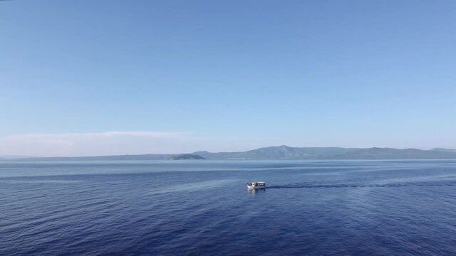 Drone flying shot following fishing boat at calm sea in Greece. Aerial top view of caique sailing at Kassandra Chalkidiki peninsula with background Sithonia view.