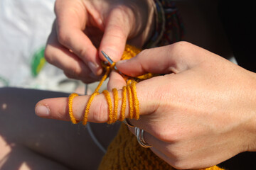 Knitting scene. Hand and knitting needles. Yellow and orange clothing.