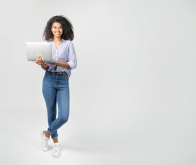 Portrait of a beautiful african woman with laptop on grey background © LumenSt