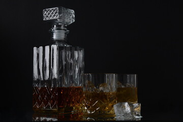 Glass of the whiskey with ice cubes and a square decanter on a black  background.