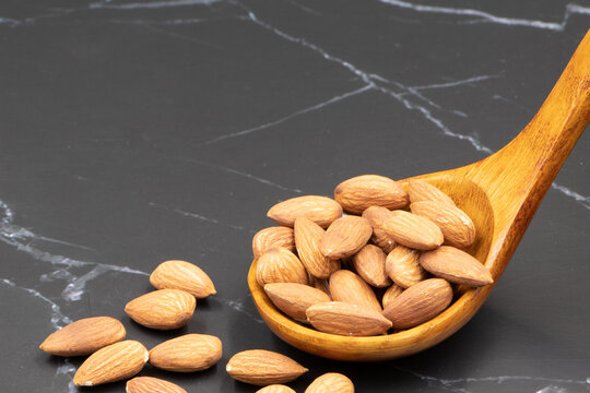 almonds on separate wooden spoons on dark stone table