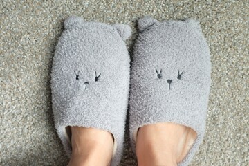 High angle shot of a person wearing a pair of cute slippers on a gray carpet