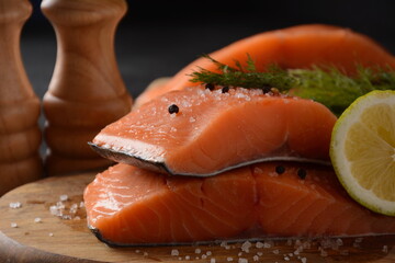Fresh raw salmon fish fillet with cooking ingredients, herbs and lemon on black background. Keto diet, unsaturated fats, omega 3, healthy nutrition. 