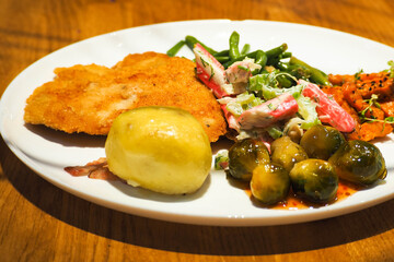 salad with crab sticks and celery stalk, sliced sweet potatoes , green asparagus pods, chops and brucelloes with sauce on a large white round plate on a wooden table in a restaurant