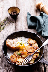 Fried Eggs and Potatoes in cast iron skillet on rustic wooden table. Skillet Breakfast. Selective focus