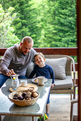 Father and son having breakfast with coffee and milk at table.Cute boy and his father enjoying time together while having breakfast.Happy dad and son talking and smiling at the table. Family bonding