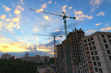 Wide-angle landscape view of construction site with two high town cranes. Construction of the new residential building. Building under construction. Beautiful sun rising sky with fantastic soft clouds