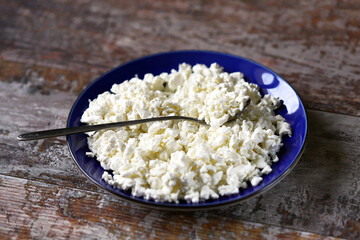 Selective focus. Freshly grained cottage cheese in a blue plate. Dairy products.