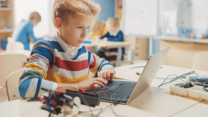 Young Schoolboy Uses Laptop to Program Software for Robotics Engineering Class. Elementary School...