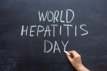 World Hepatitis day text on a chalkboard, hand with chalk