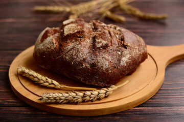 Dark rye bread on a light wooden board on a brown wooden table.