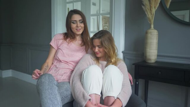 two girls friends sit at home on a chair and talk. girls spend time together at home