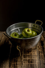 green apples in aluminum strainer on wood