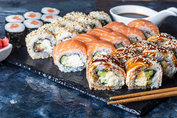 A box of sushi Nigiri, Uramaki California, Philadelphia, on a black stone plate. Sushi menu in a white transport box on a wooden background.