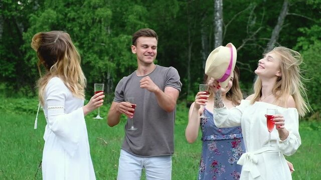 group happy cheerful laughing young friends enjoy country picnic in forest in clearing on summer day. people dance outside house with red wine drink cocktail have fun spend active holidays in nature