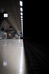 A well lit train station in the underground seperated by a leading line in the center from the dark and dirty rails.