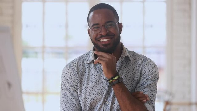 Happy young black businessman entrepreneur looking at camera in office, smiling positive african american guy startup owner designer laughing posing in work space, close up business portrait