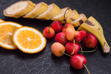 yellow cherries, sliced orange and banana on a dark background