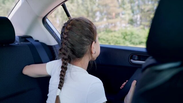 Sad young girl in a white T-shirt in the back seat of a car that drives on a bumpy road. A girl looks out the window of a car