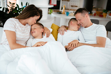 Fototapeta na wymiar Young family enjoying in bed. Happy parents with sons relaxing in bed. 