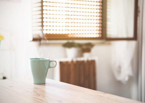 Closeup of a cup of hot coffee with the steam coming out - Cup of tea on a wooden table in a domestic kitchen - warm vintage filter.