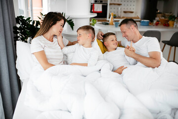 Young family enjoying in bed. Happy parents with sons relaxing in bed.	
