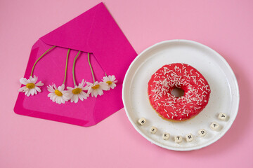 Flowers in an envelope and a donut on a pink background