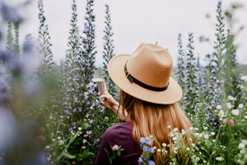 Beautiful girl in brown hat among purple wildflowers in field. Concept of freedom, travel,...