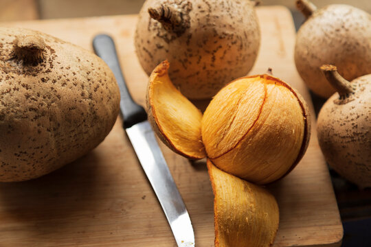 a partially peeled mammee apple (Mammea americana) fruit among others with a knife lying near